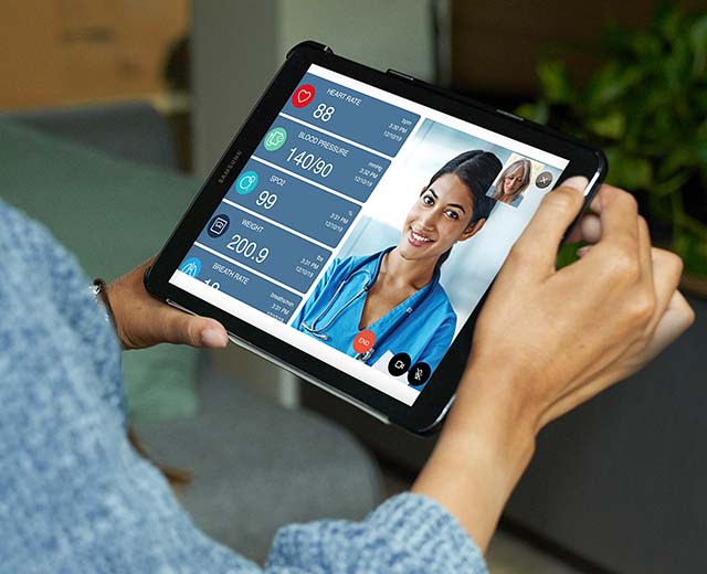 Person holding a Remote Patient Monitor featuring a woman talking to a patient through the screen